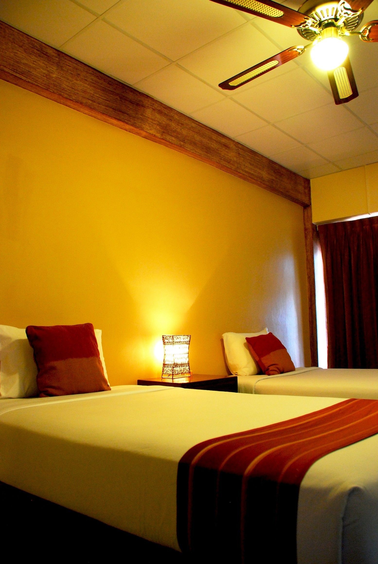 A hotel room with two beds, a ceiling fan, and a nightstand with a lamp.