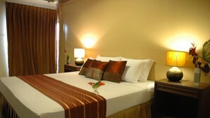 A hotel room with a large bed, a bedside table with a lamp, and a nightstand with a vase of flowers. - DMa Hotel (Khon Kaen)