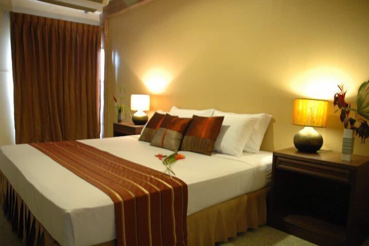 Une chambre d’hôtel avec un grand lit, une table de chevet avec une lampe et une petite table de nuit ornée d’un vase de fleurs.