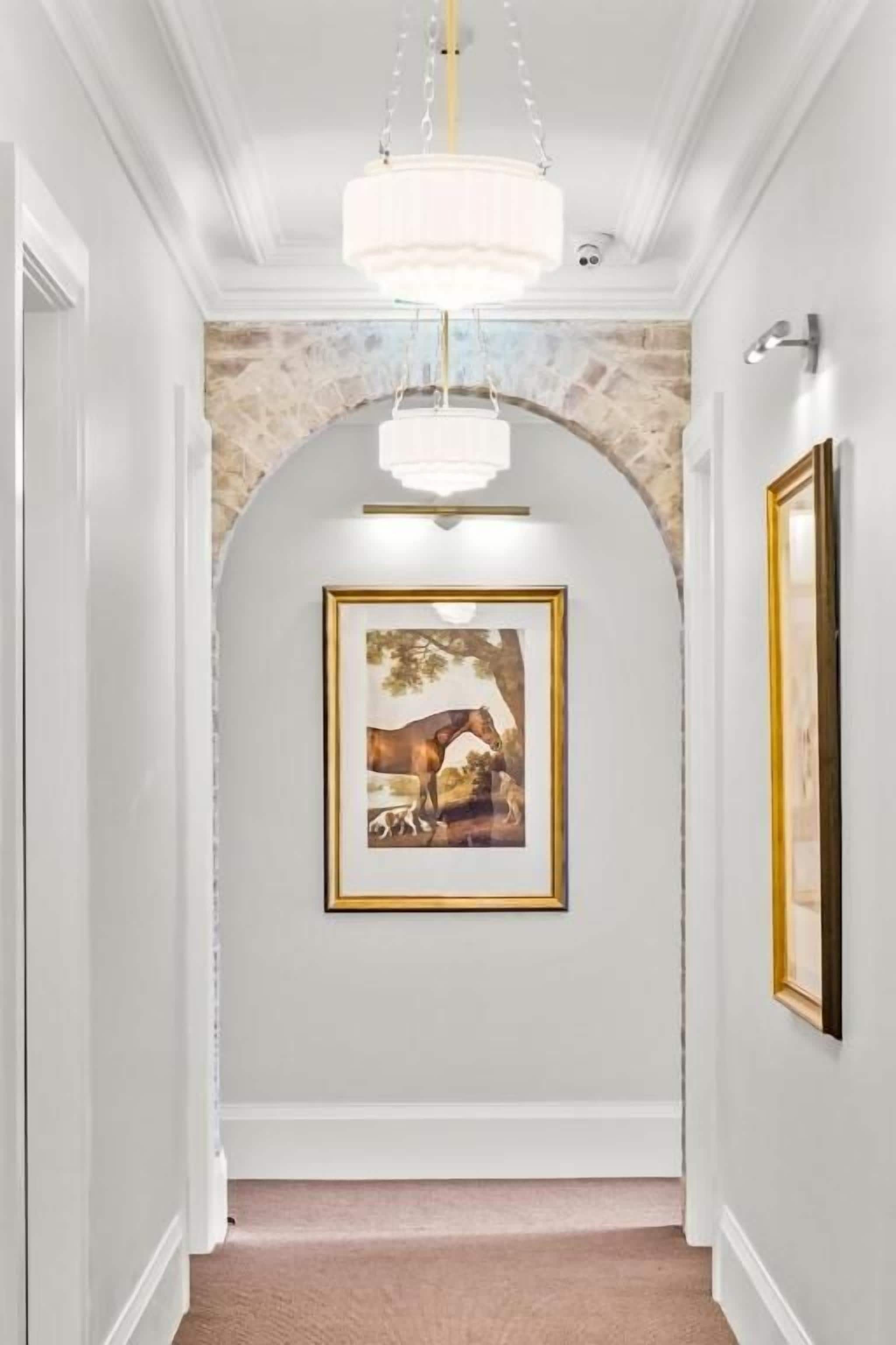 Ein Flur mit einer Chandelüster, einem gerahmten Bild an der Wand und einem steinernen Bogen.