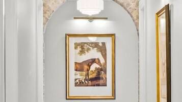 Ein Flur mit einer Chandelüster, einem gerahmten Bild an der Wand und einem steinernen Bogen.