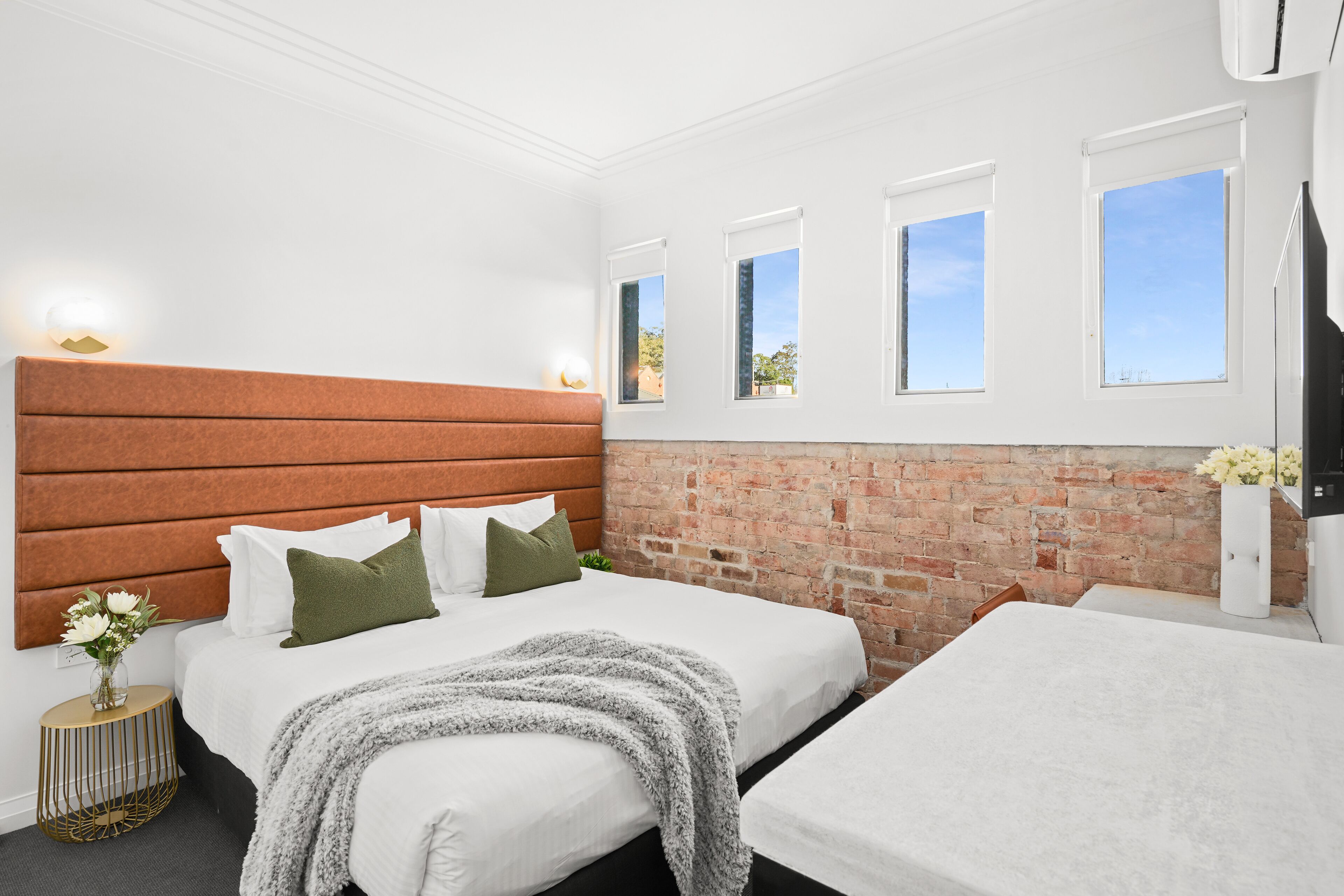 A hotel room with two beds, a brick wall, and a large window.