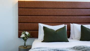 A neatly made bed with a striped blanket, a brown headboard, and two green pillows.