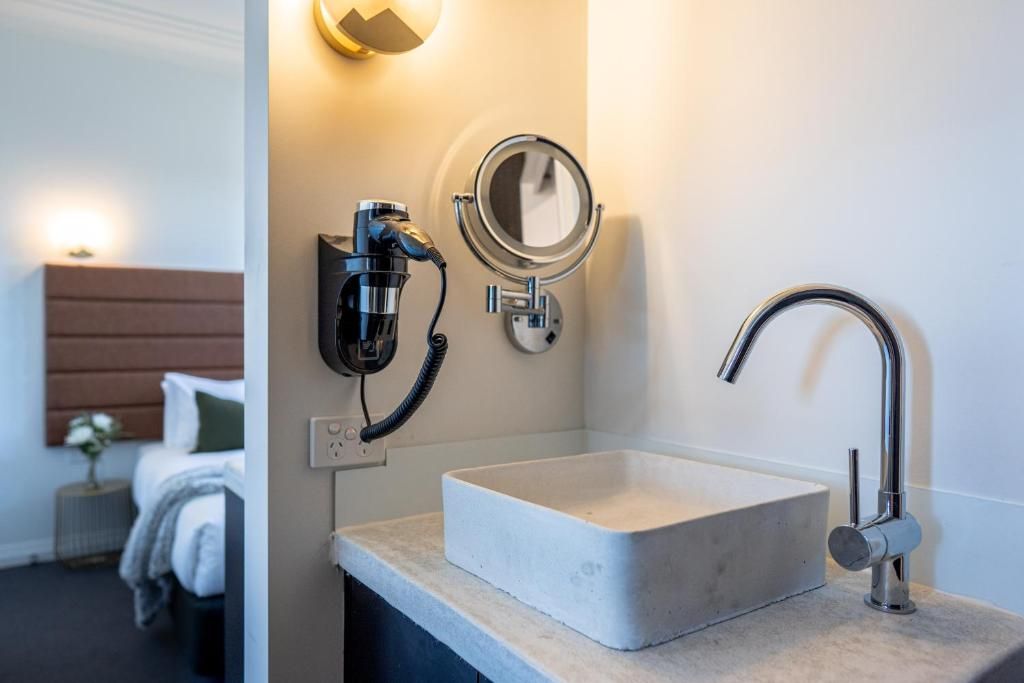 A bathroom with a rectangular sink, a handheld showerhead, a wall-mounted mirror, and a light fixture.