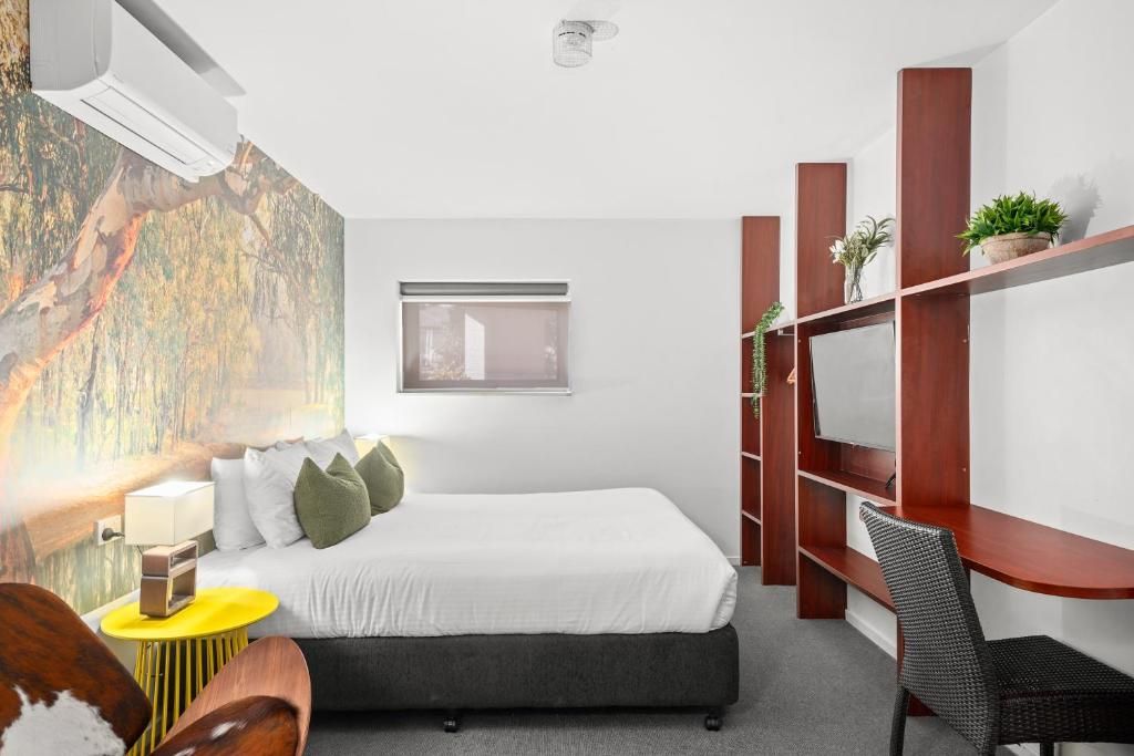 A modern hotel room with a bed, a desk, a chair, a TV, and a window.