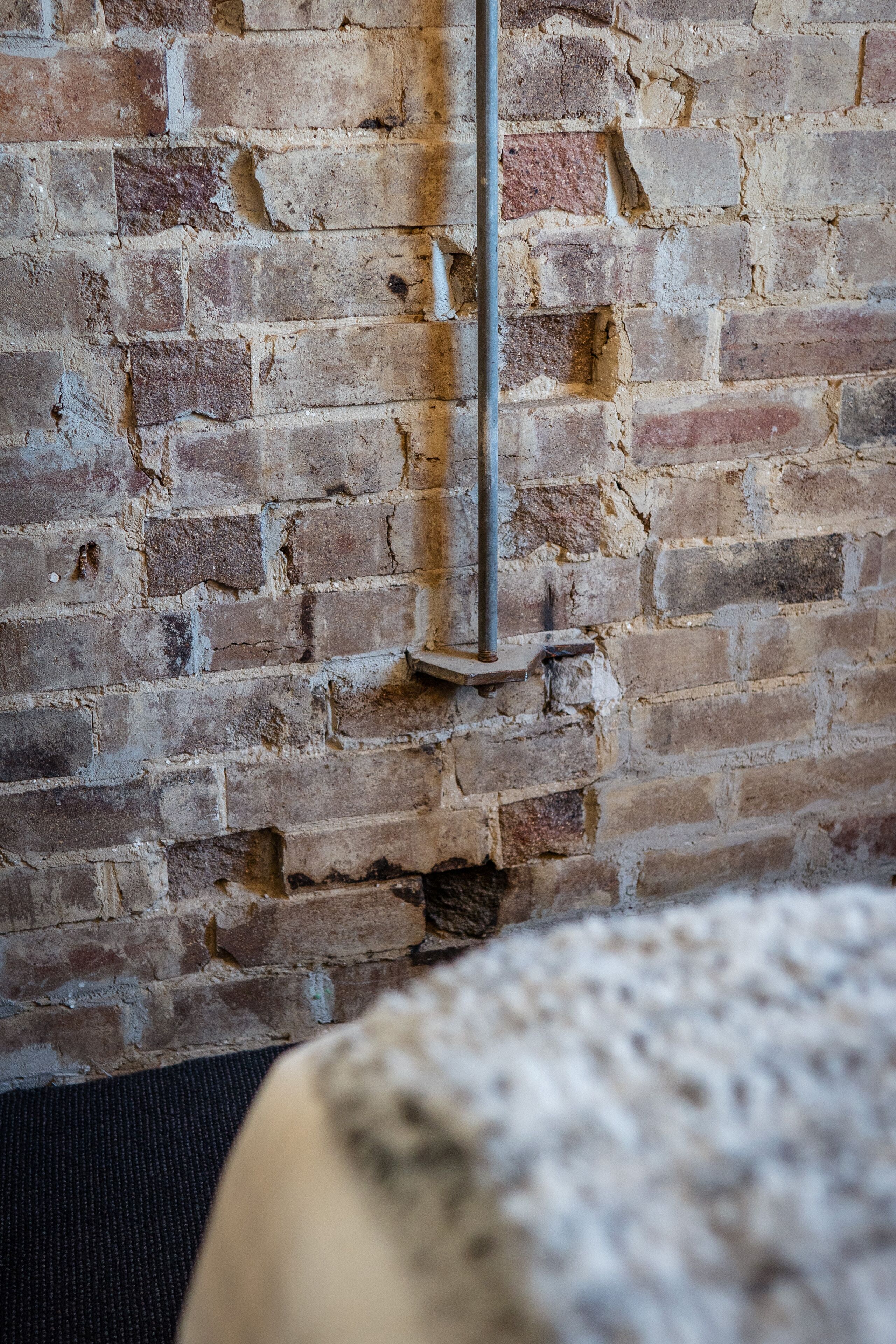 A brick wall with a metal pole and a small shelf.