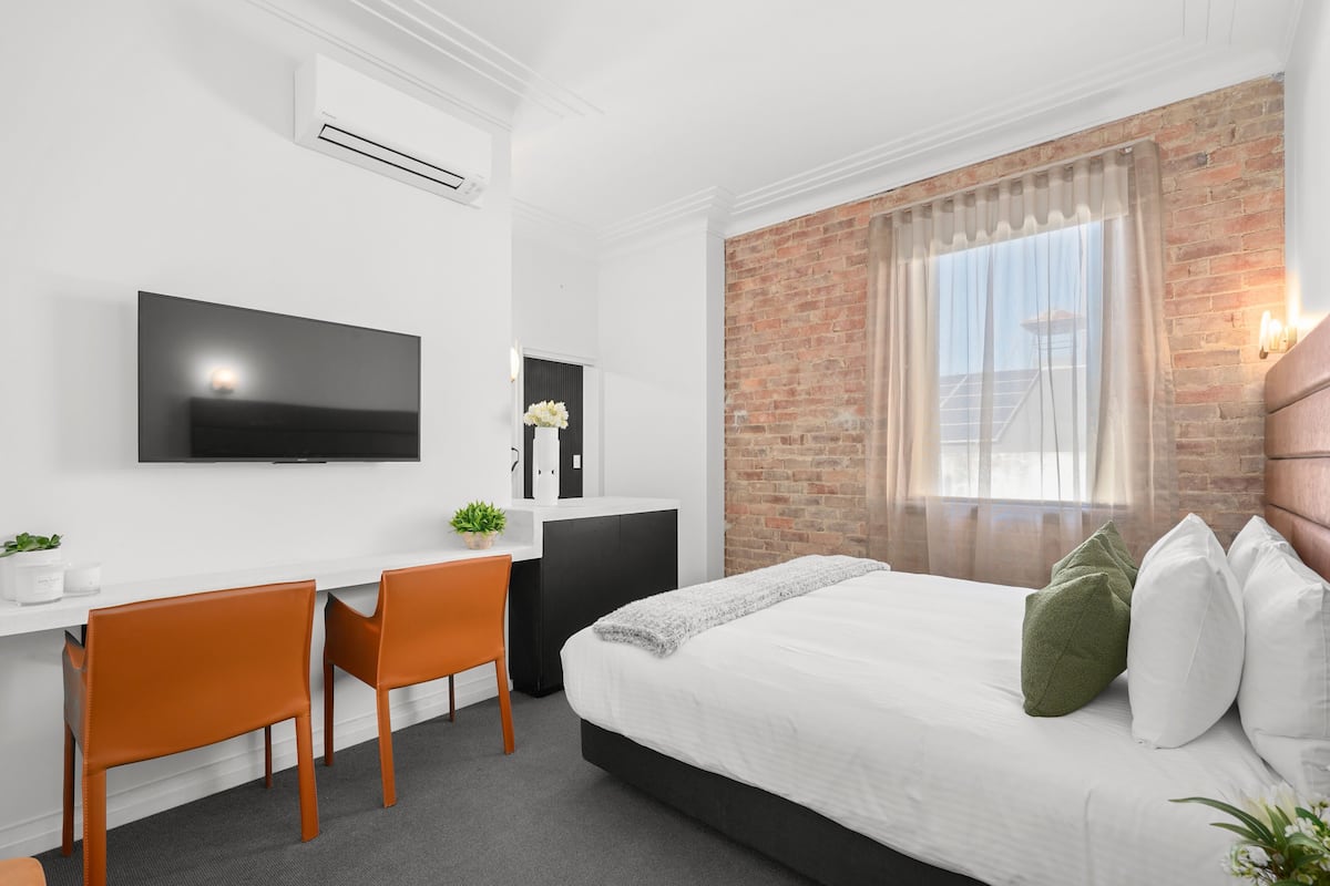 Habitació d'hotel moderna amb un llit gran, una escriptori, dues cadires, un televisió de pantalla plana i una paret de maó.