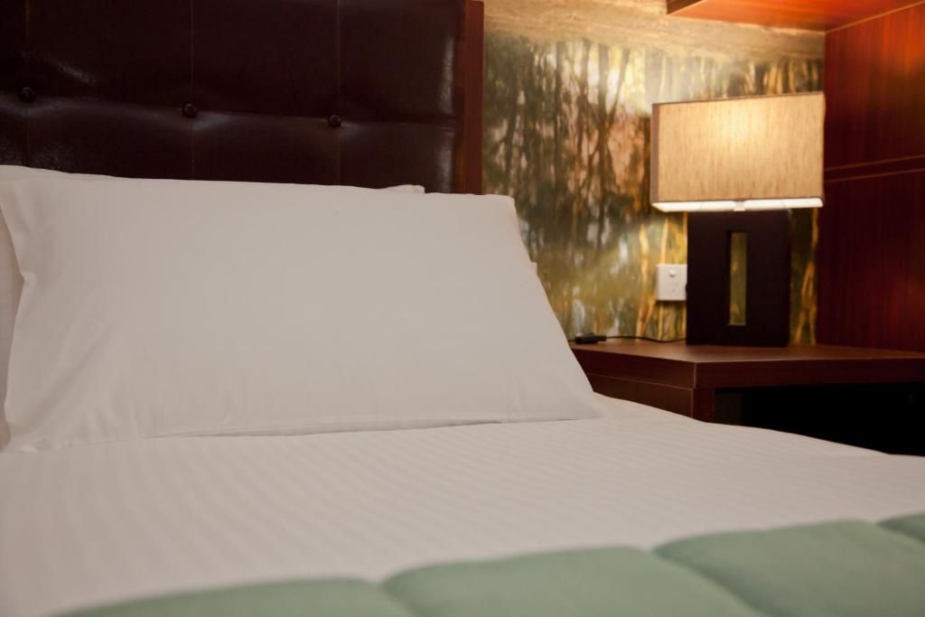 Una habitación de hotel con una cama, una mesita de noche y una lámpara.