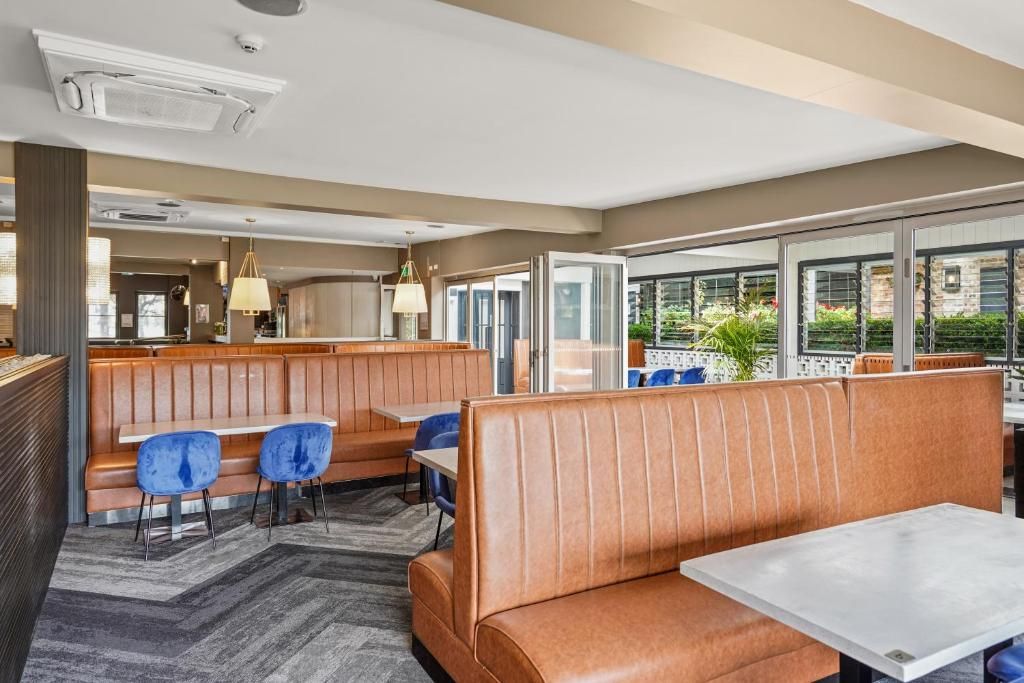 A modern restaurant with leather booths, blue chairs, and a view of greenery outside.