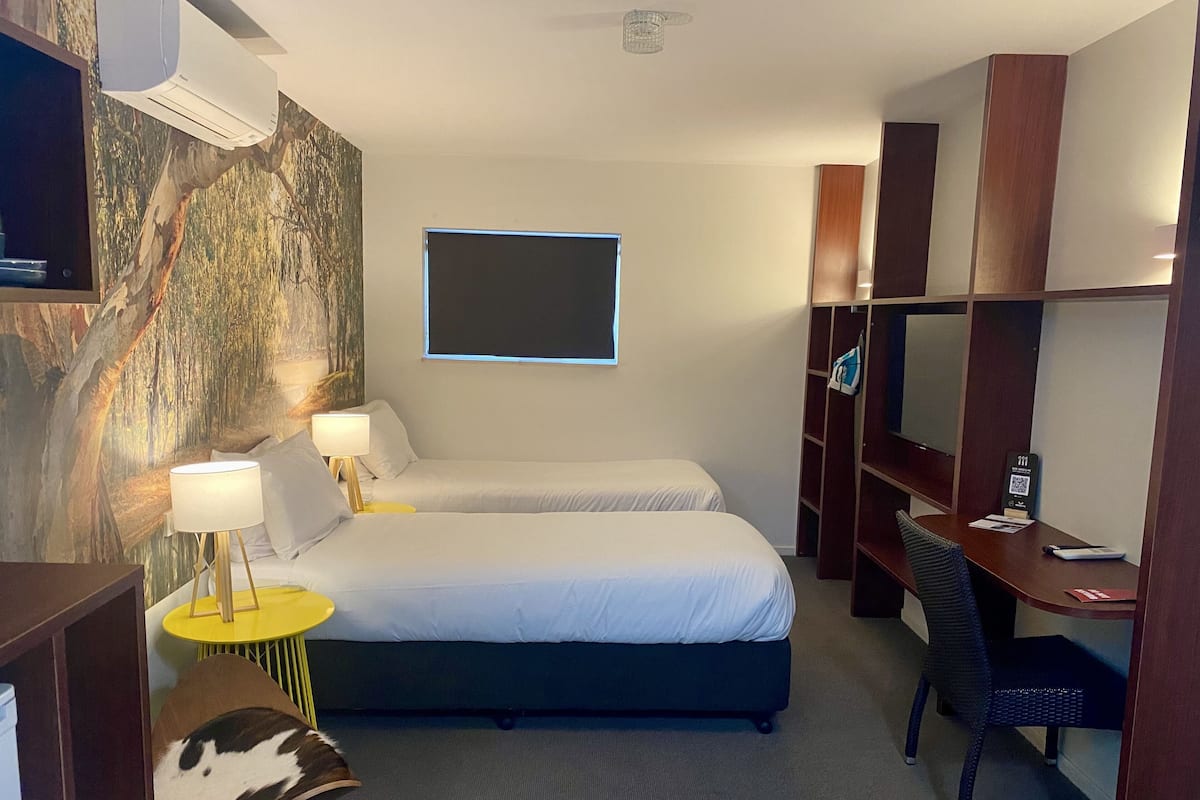 Habitació d'hotel amb dos llits, un escriptori, una cadira, un televisor i aire condicionat fixat a la paret.
