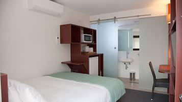 A hotel room with a bed, a desk with a microwave, a chair, and a bathroom visible through an open door.