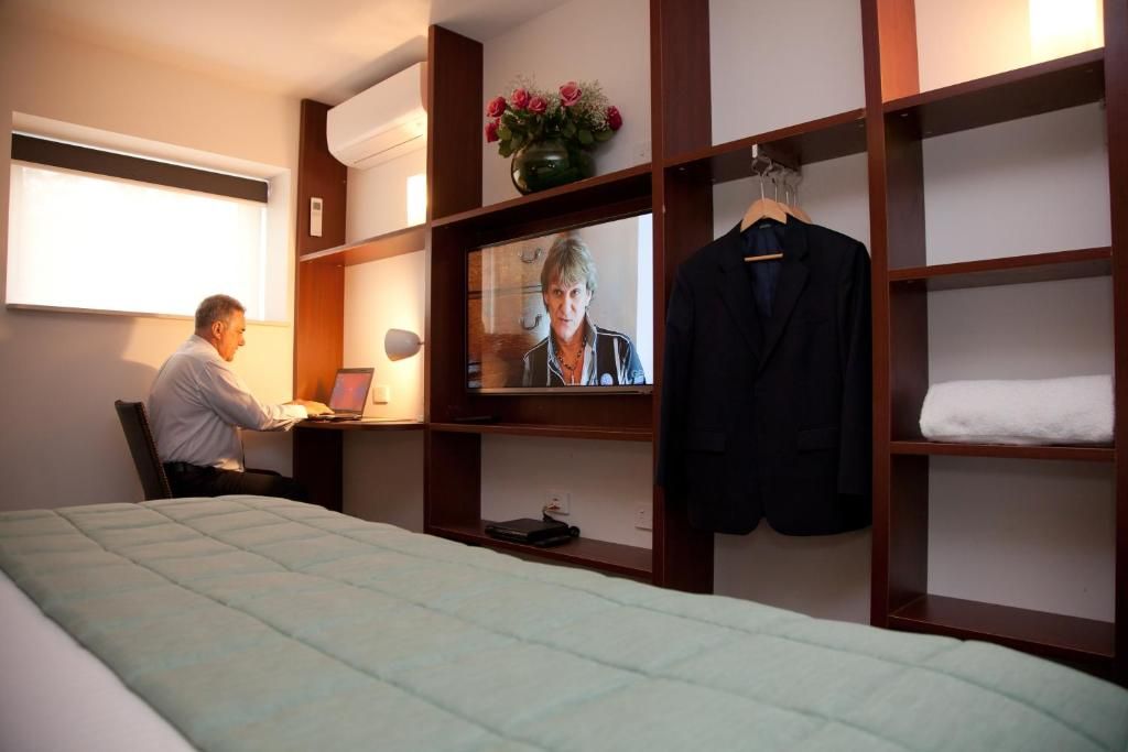 Een hotelkamer met een bed, een bureau met een laptop, een televisie en een kledingkast.
