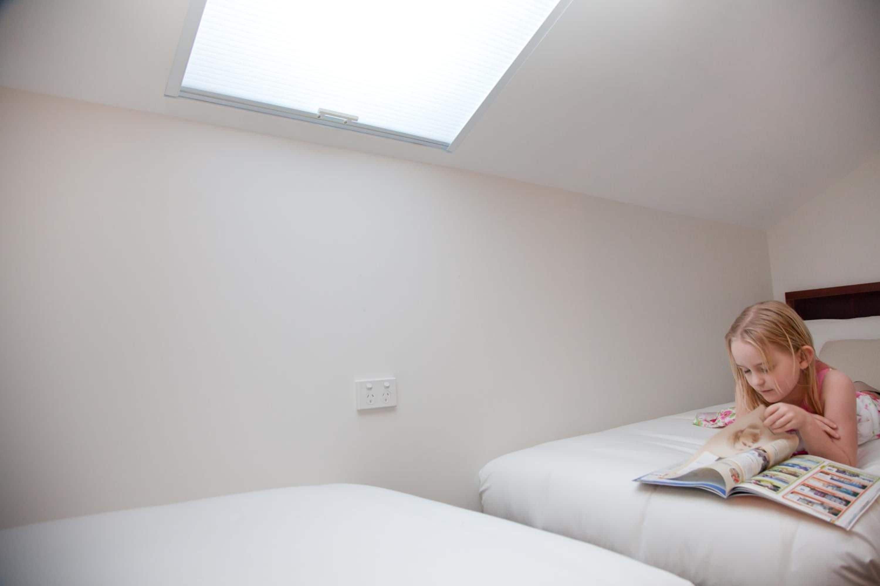 Une pièce avec une lucarne, un lit et une personne qui lit un magazine.
