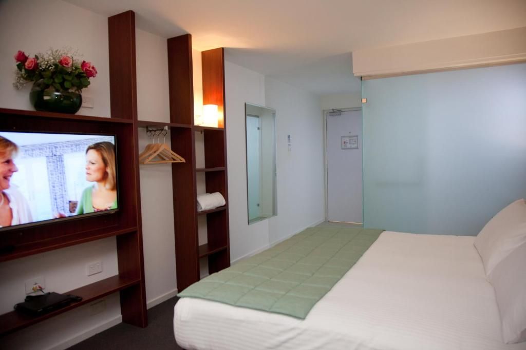 Ein Hotelzimmer mit Bett, Fernseher, Spiegel, Kleiderschrank und Tür.