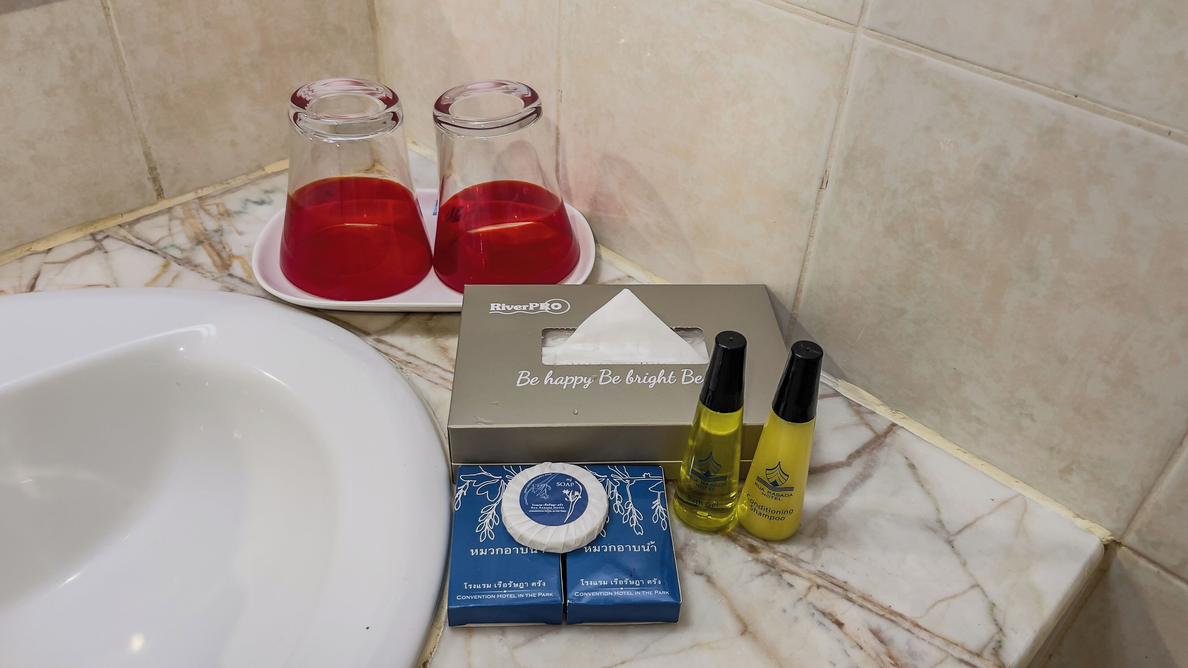 A bathroom with a sink, two glass bottles with red liquid, a soap dispenser, and two yellow shampoo bottles.