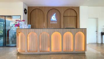 A reception desk with a wooden finish and illuminated panels, a logo above the desk, and a small display of brochures and a vase with flowers.