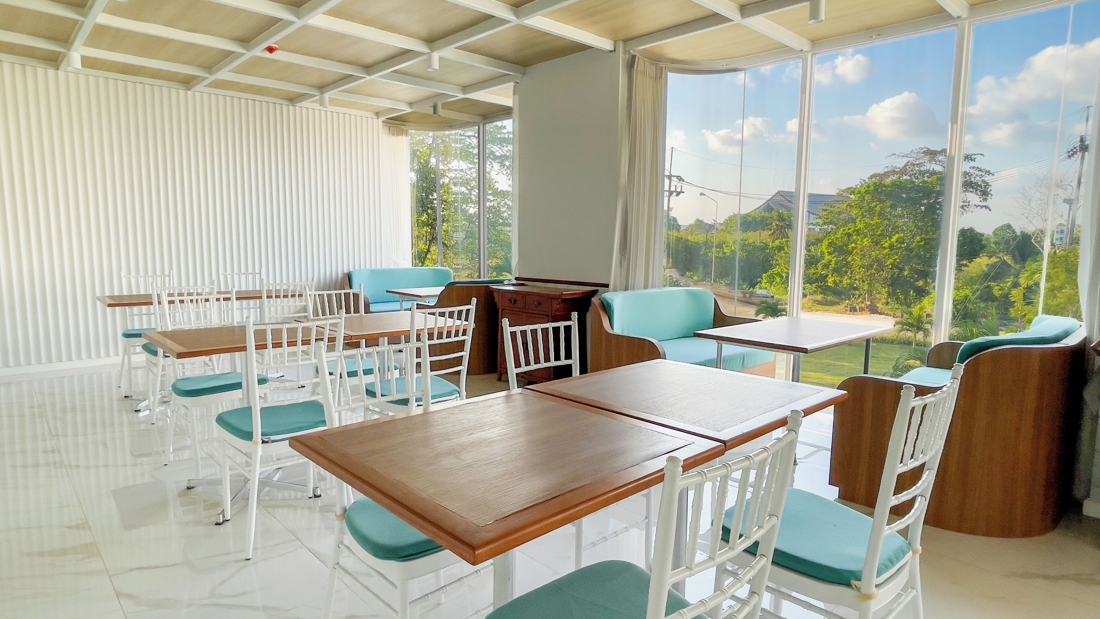 Un comedor moderno con sillas blancas y mesas de madera, grandes ventanas que ofrecen vistas a la vegetación.