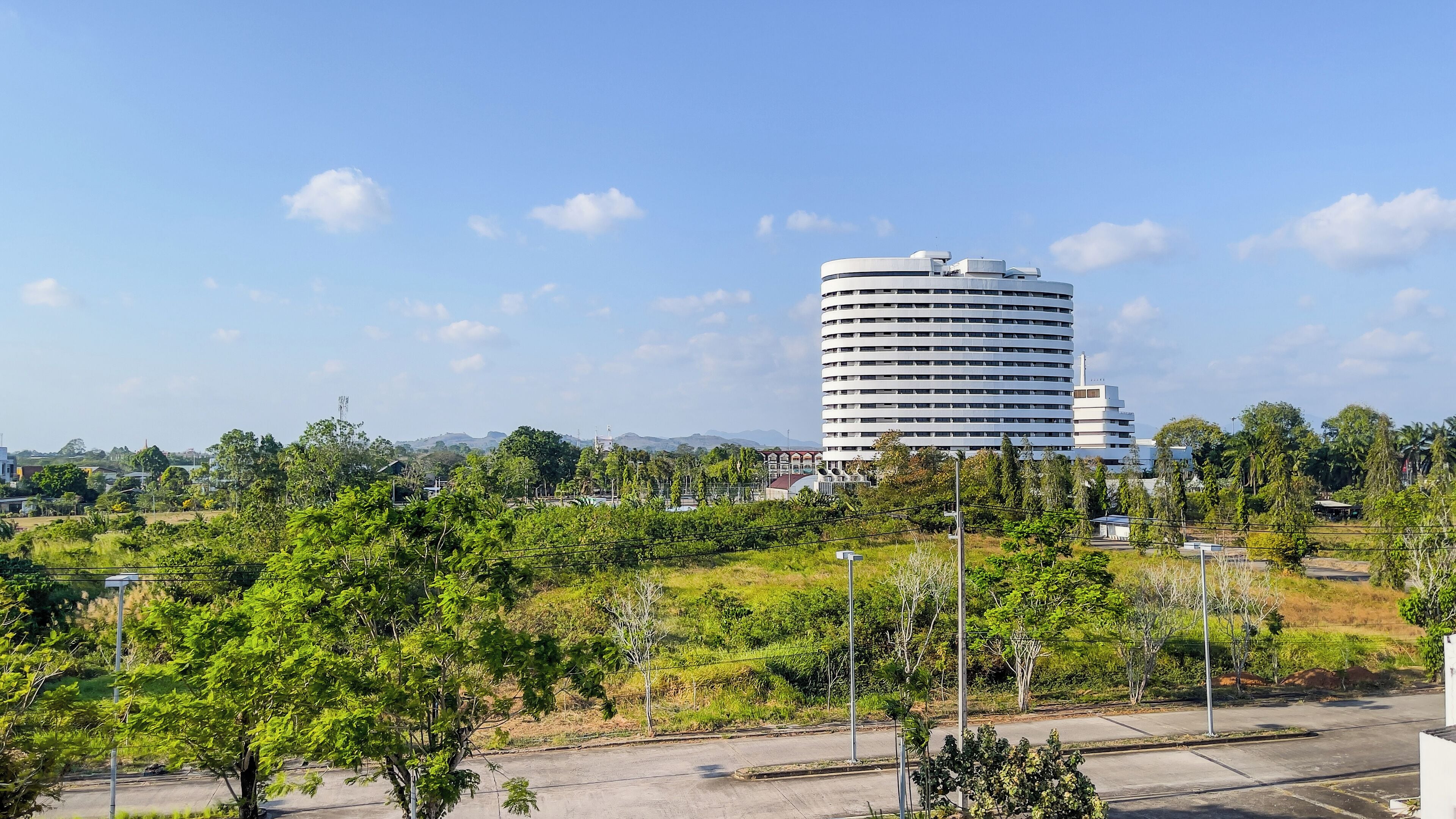 A modern building with a circular design, surrounded by greenery and a clear sky.