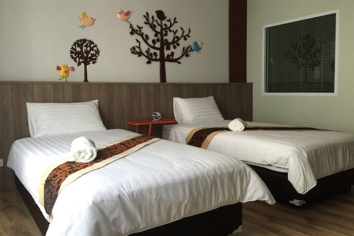 Een hotelkamer met twee bedden, een houten hoofdeinde, een muur met decoratie van bomen en vogels, en een raam met luxaflex.