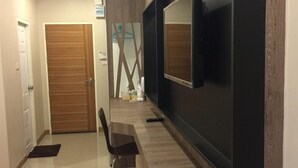 Una sala de estar moderna con un televisor de pantalla plana montado en una pared oscura, una puerta de madera y una zona de comedor con un banco y una silla.