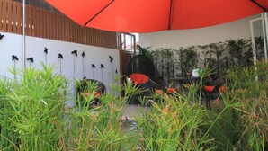 Un área de estar al aire libre con un amplio paraguas naranja, una valla de madera y una pared decorada con motivos de pájaros.