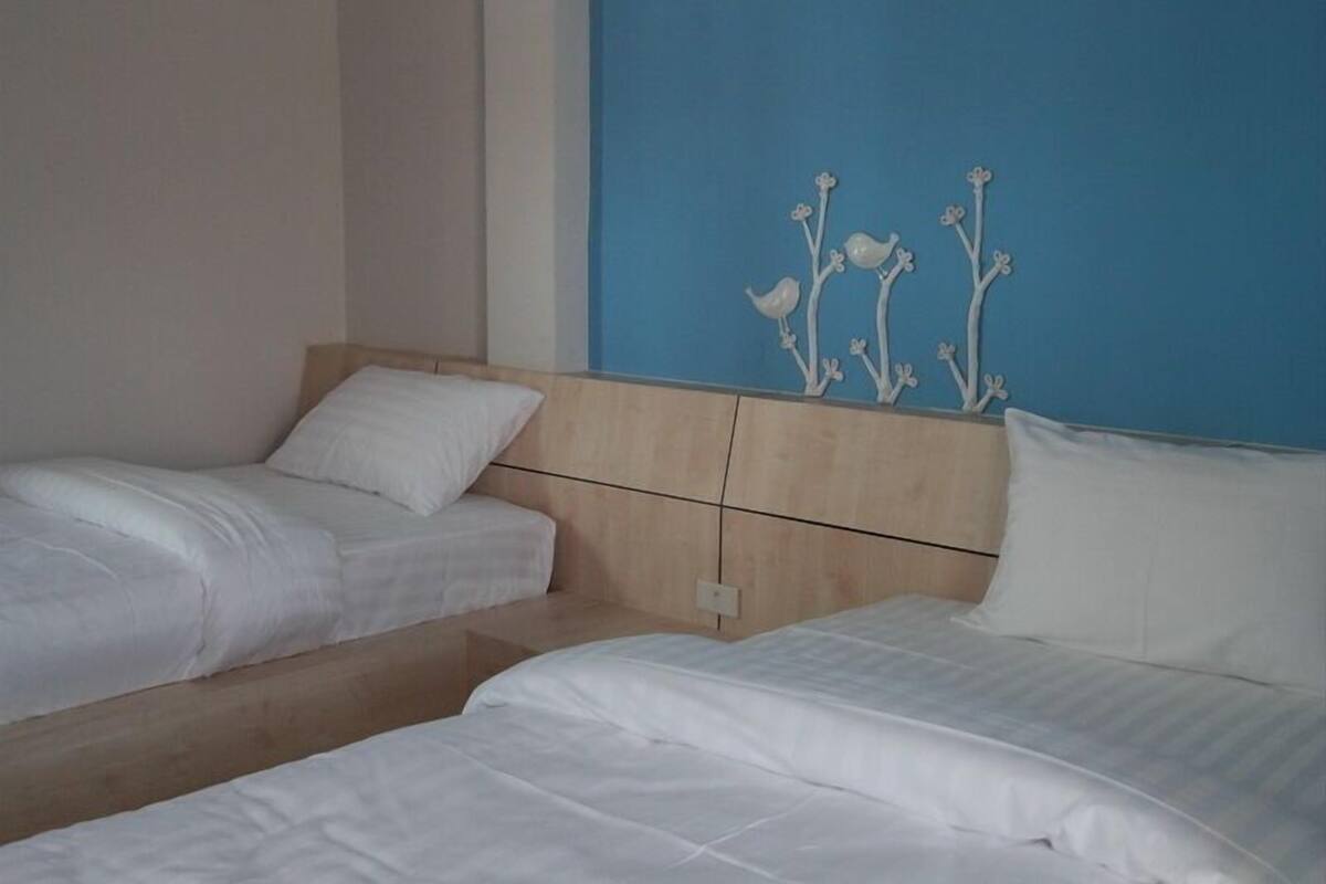Een hotelkamer met twee eenpersoonsbedden, een houten hoofdbord en een blauwe accentmuur met bloemdecoratie.