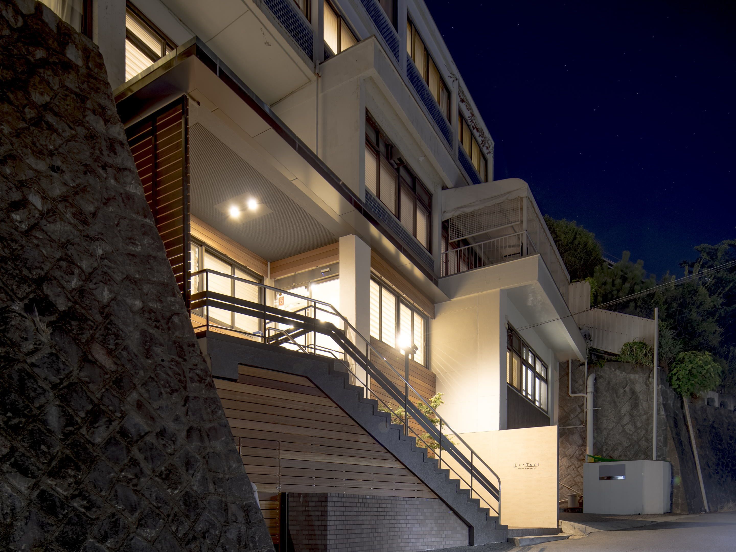 Ein modernes Gebäude mit einer Treppe, die zu einem Balkon führt, einer Steinmauer und einem Schild mit der Aufschrift 'LeTore'.