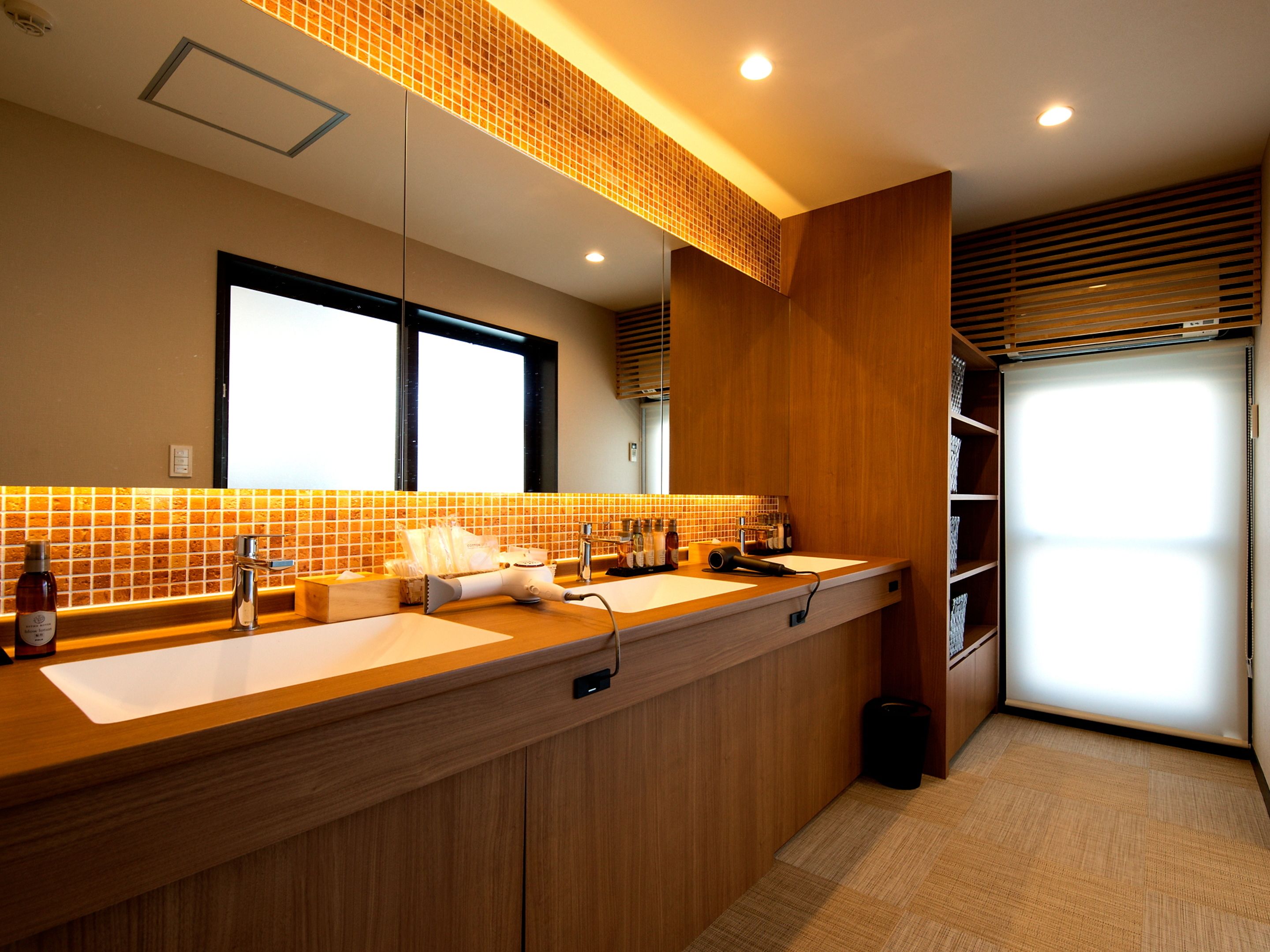 A modern bathroom with a wooden vanity, two sinks, a mirror, and a window.