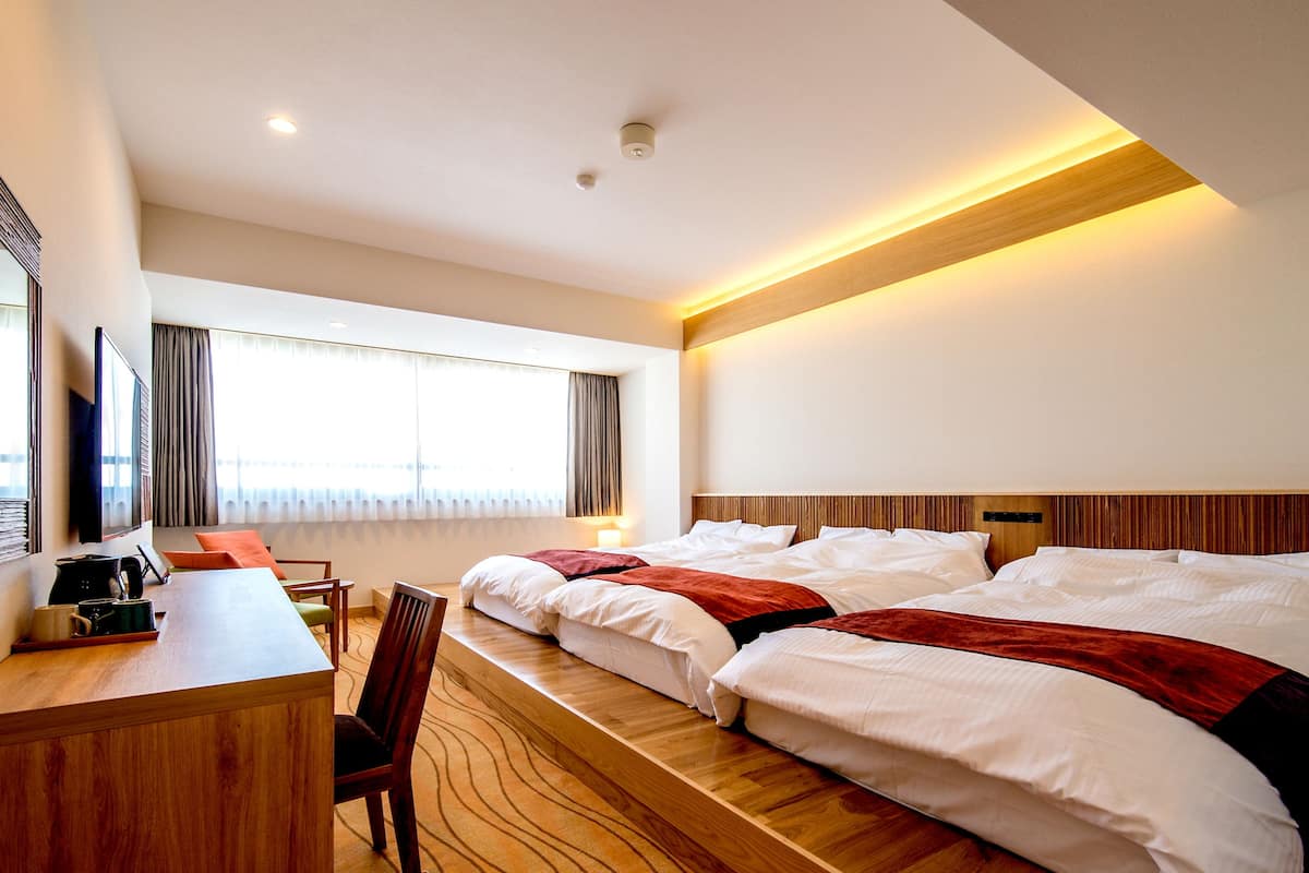 A hotel room with two beds, a desk, and a TV.