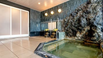 Wellnessbereich mit einer großen Felsformation, einer gläsernen Whirlwanne und einem modernen Badezimmer mit schwarzer Ablage und weißen Armaturen.