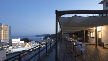 Una terraza con asientos al aire libre, con vistas a un paisaje urbano y al mar.