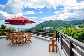 A terrace with wooden furniture and a red umbrella, overlooking a green hillside and a distant town. - Lectore Atami Koarashi (TKP Hotels & Resorts) (Atami)