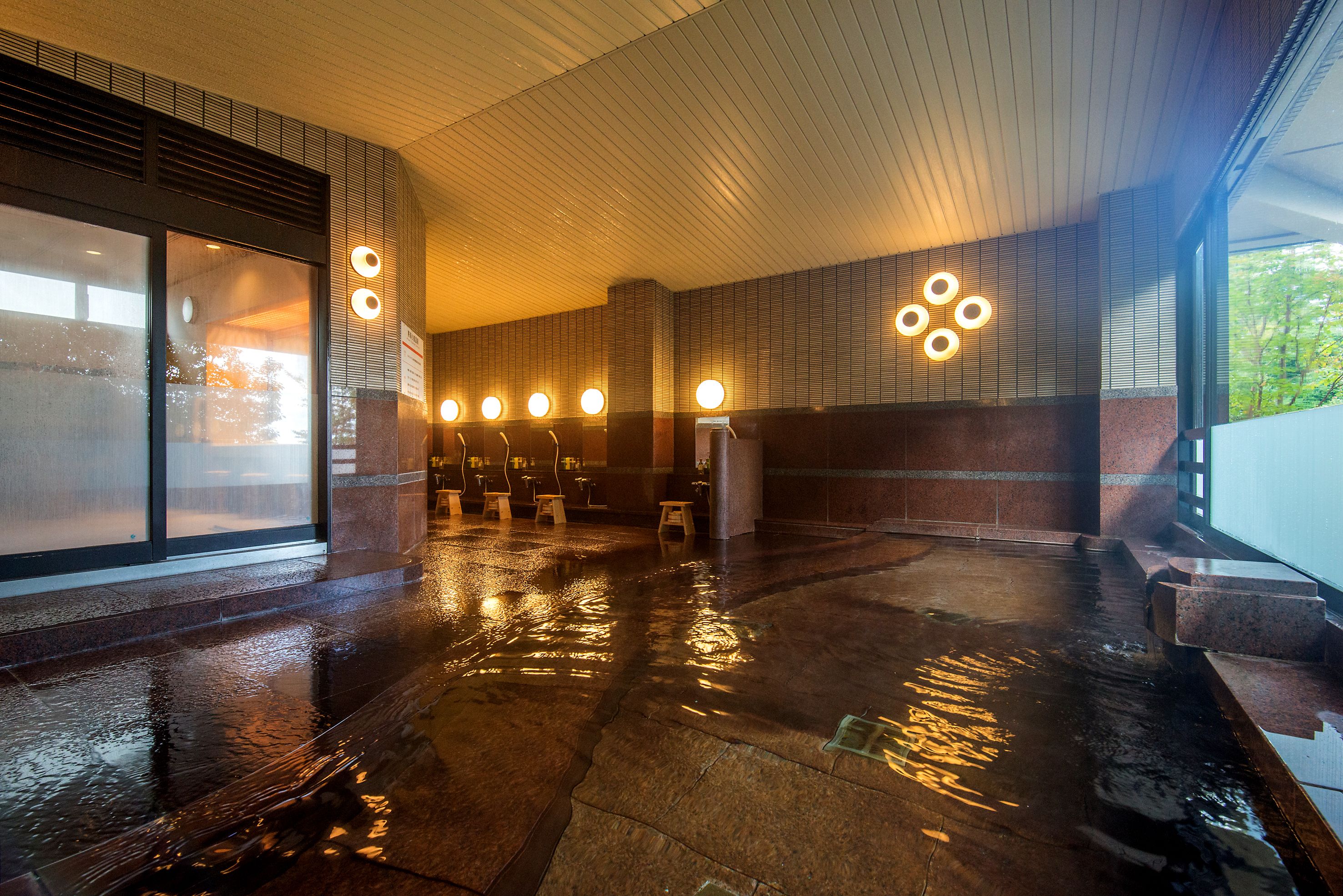 A wet floor in a modern building with a glass entrance, a seating area, and a wall with circular light fixtures.