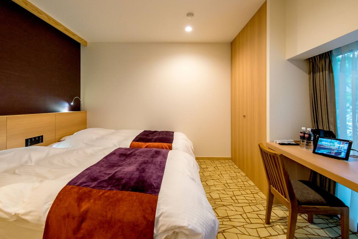 A hotel room with two beds, a desk, a chair, and a television.