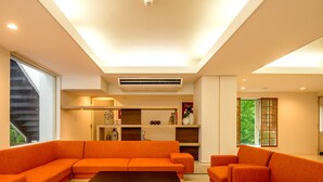 A modern living room with orange sofas, a black coffee table, and a built-in air conditioning unit. - TKP Hotel & Resort Lectore Hakone Gora (Hakone)