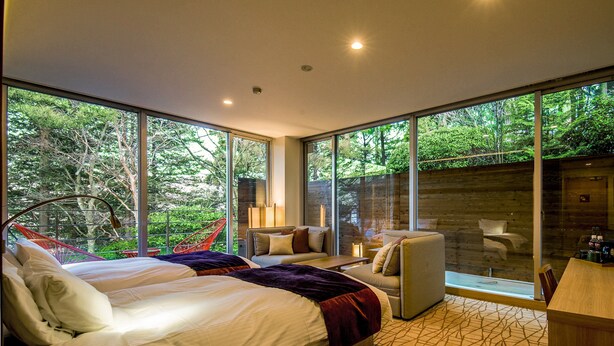 A modern bedroom with a large bed, a seating area with a chair and a table, and large windows offering a view of the outdoors. - TKP Hotel & Resort Lectore Hakone Gora (Hakone)
