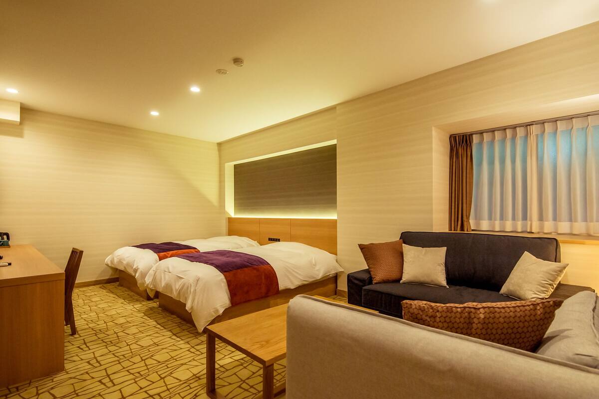 A hotel room with a bed, a sofa, a desk, and a patterned carpet.
