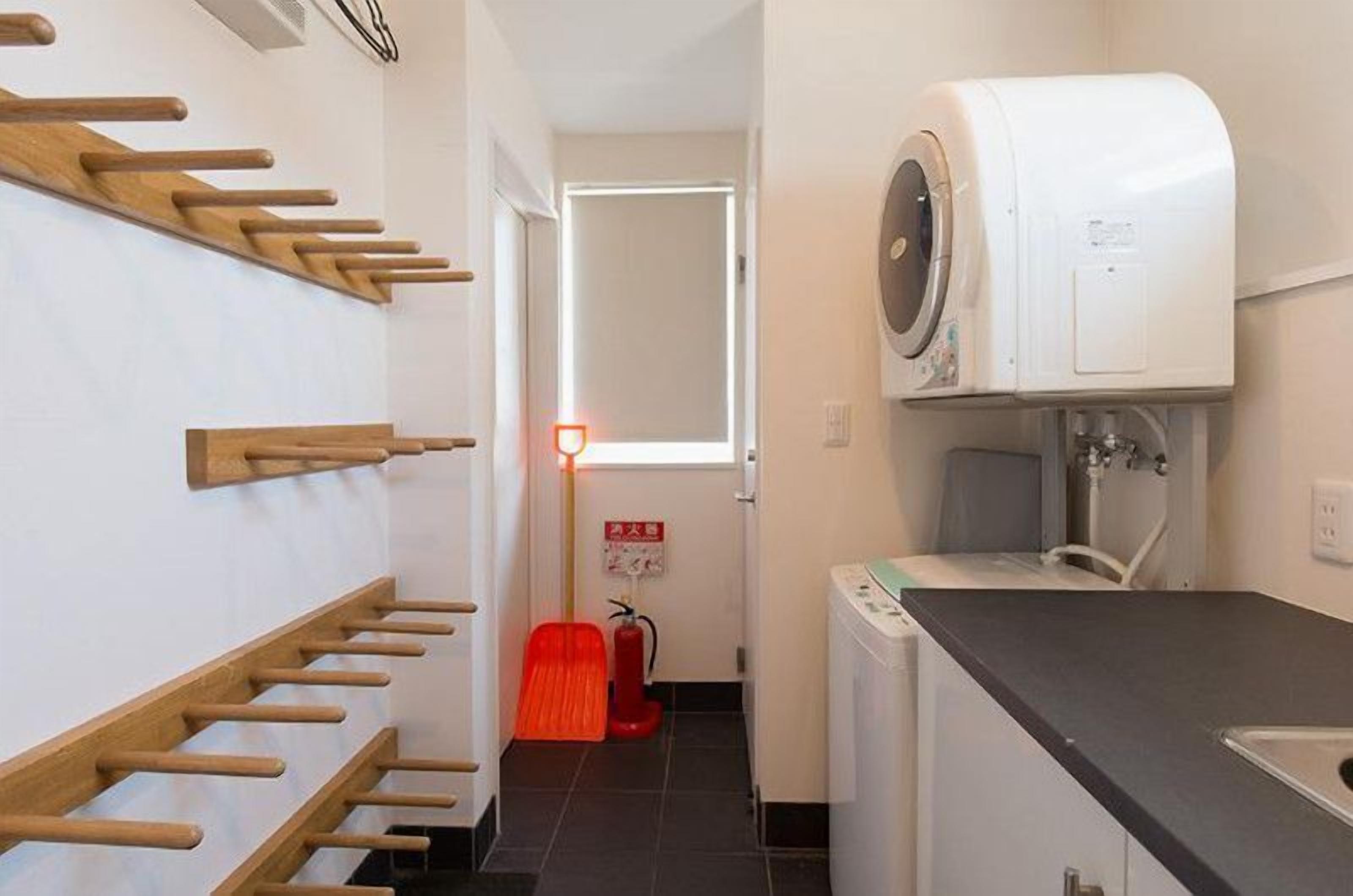 Un couloir étroit, avec des patères en bois fixées au mur sur le côté gauche, un lave-linge sur le côté droit et un extincteur au centre.