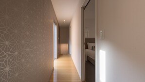Un pasillo con papel tapiz estampado, suelo de madera y una cama con almohadones.