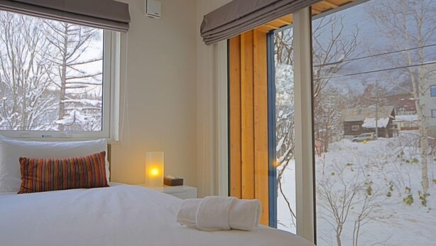 Habitación de hotel con cama, lámpara de noche y ventana con vista a un paisaje nevado.