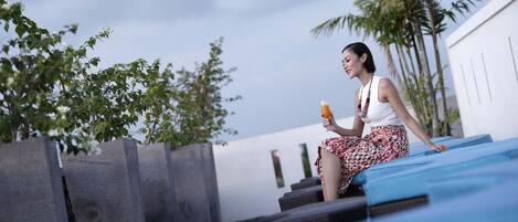 A person sitting on a blue lounge chair outdoors, holding a drink.