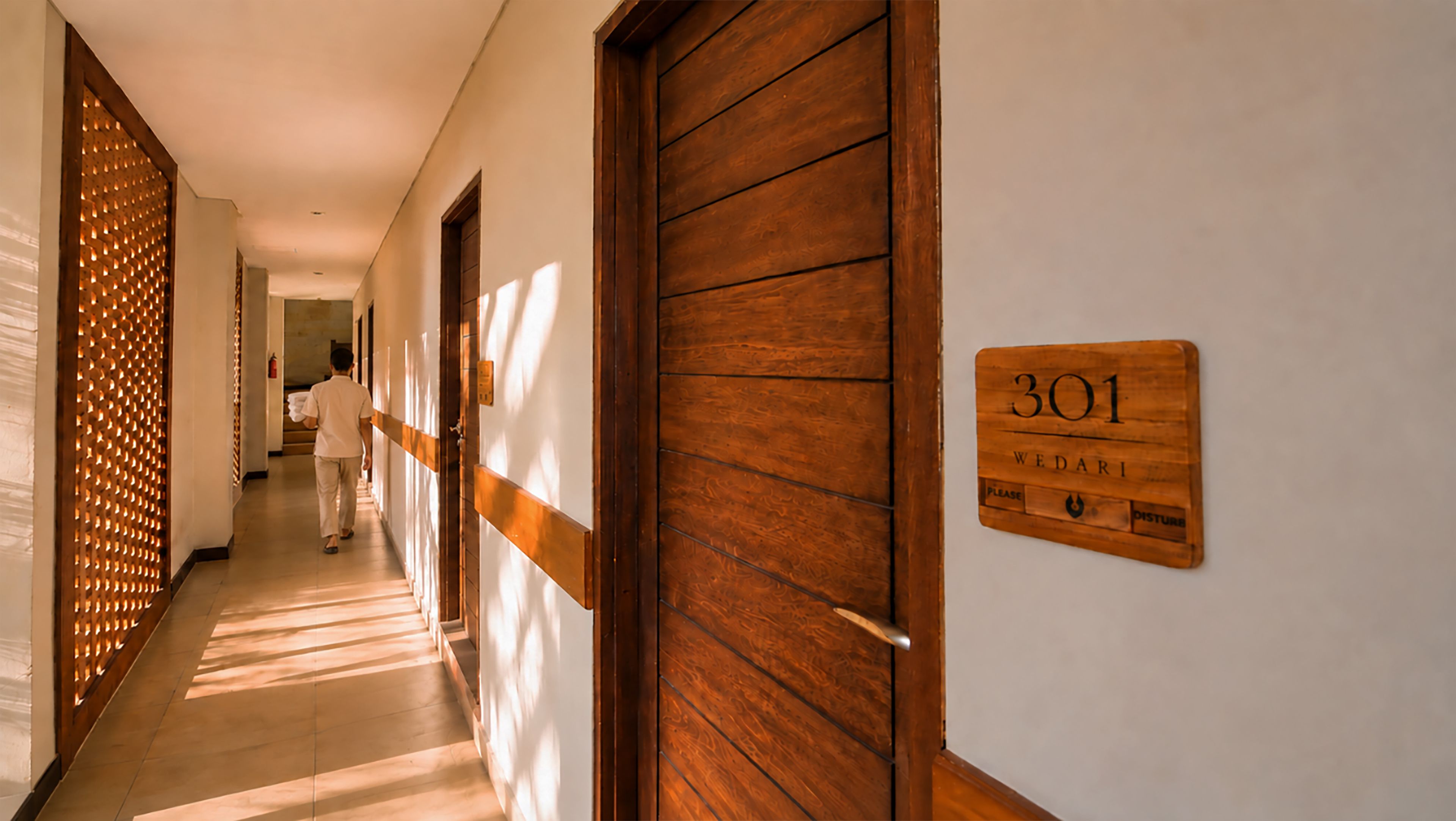 A hotel corridor with wooden doors, a sign indicating room number 301, and a person walking down the hallway.