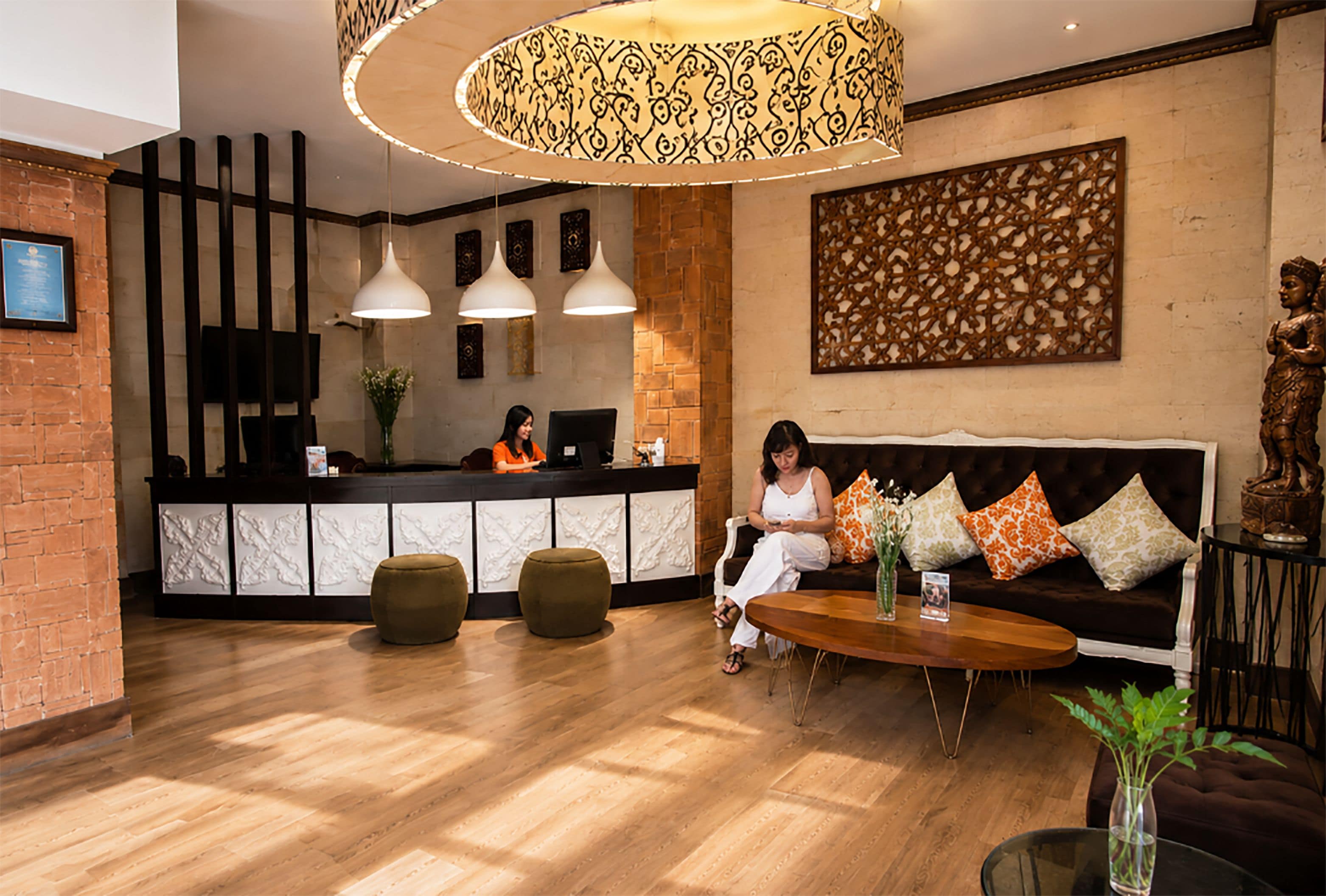A reception area with a wooden floor, a reception desk, two pendant lights, a sofa with cushions, and a statue.