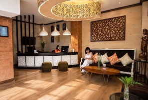 A reception area with a wooden floor, a reception desk, two pendant lights, a sofa with cushions, and a statue. - The Visala Boutique Hotel (Keroboken Kelod)