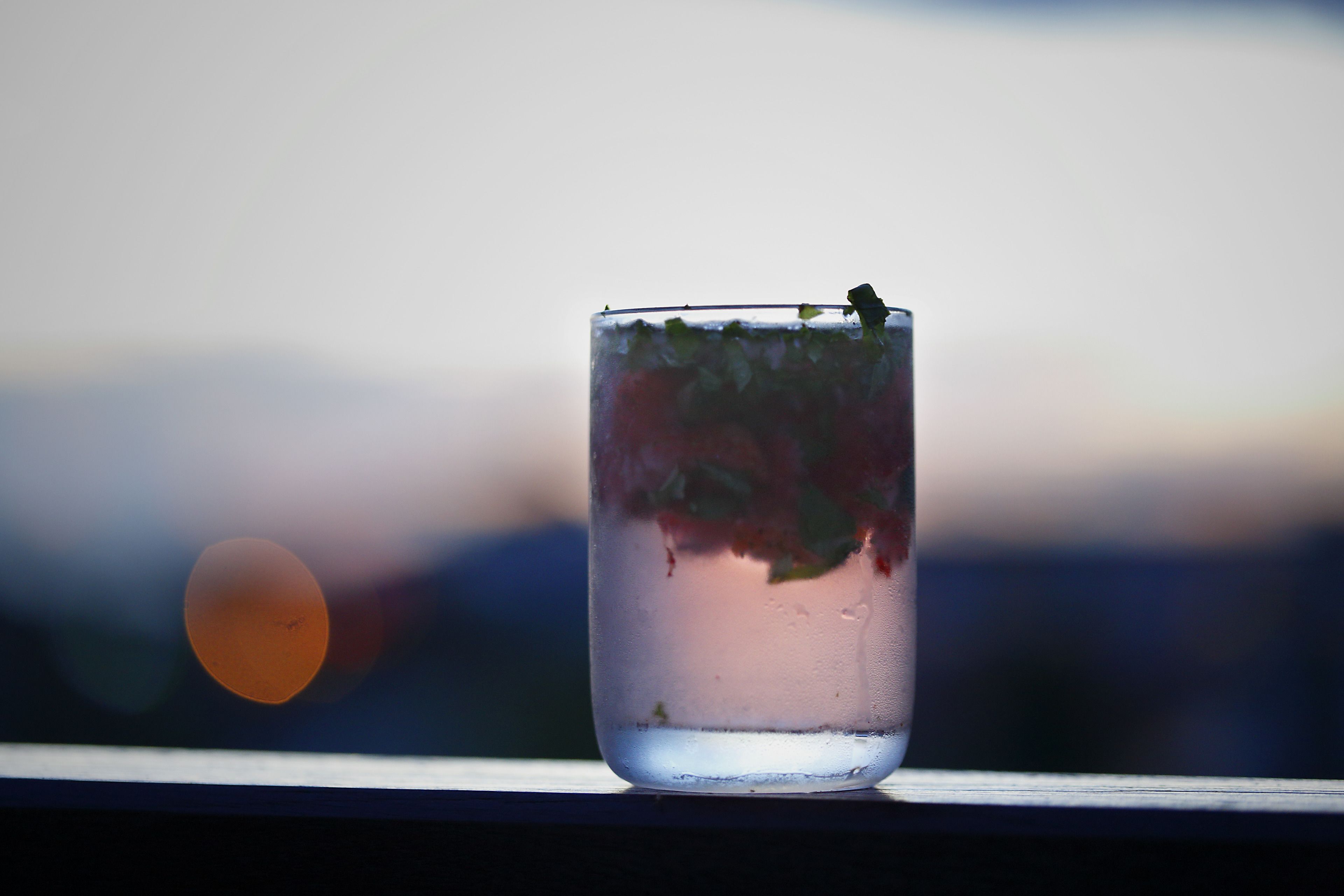 A glass of water with mint leaves on a windowsill.