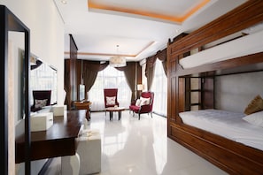 A hotel room with a bunk bed, a desk with drawers, two armchairs, a round table, and a chandelier.