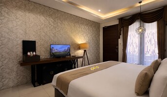 Una camera d'albergo con un letto, una televisione su un mobile, una scrivania con una lampada e una finestra con tende.