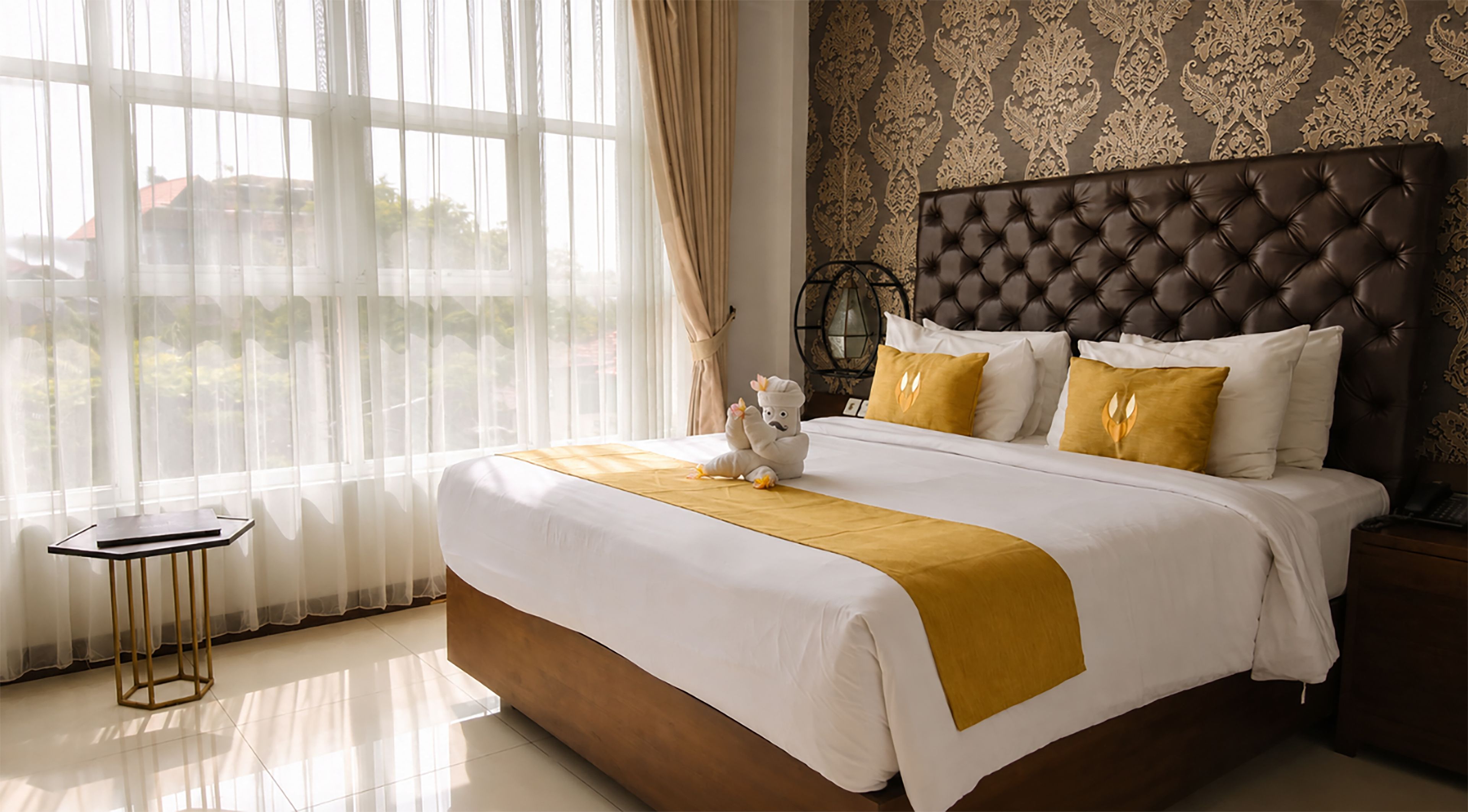 A hotel room with a large bed, a bedside table, a decorative wall, and a view through the window.