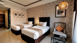 A hotel room with two beds, a chair, a bedside table, a lamp, and framed pictures on the wall. - The Visala Boutique Hotel (Keroboken Kelod)
