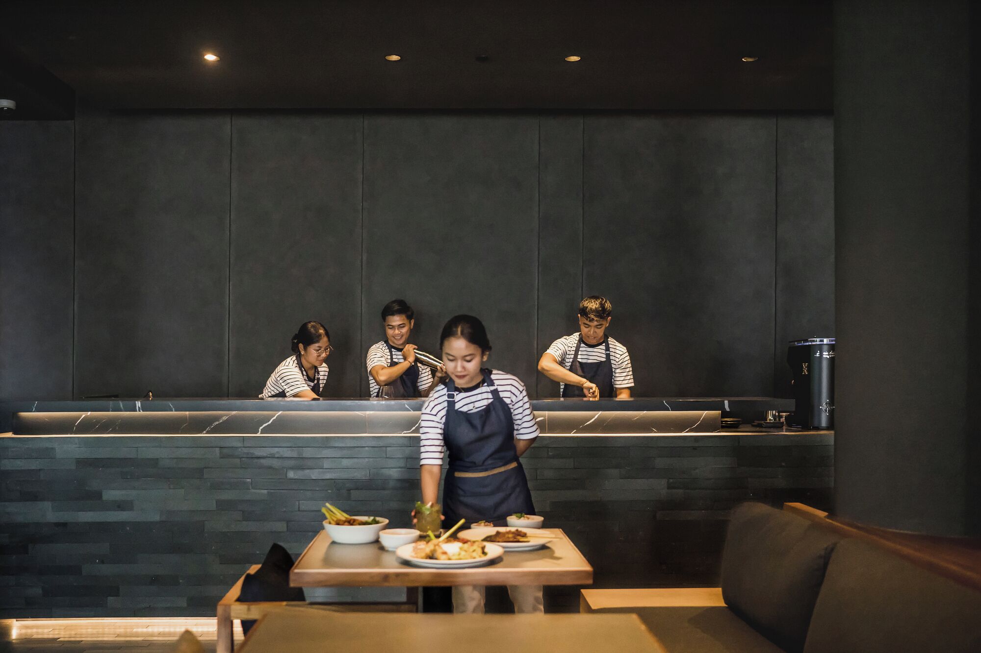 A restaurant interior with a counter, four staff members, and a table with dishes.